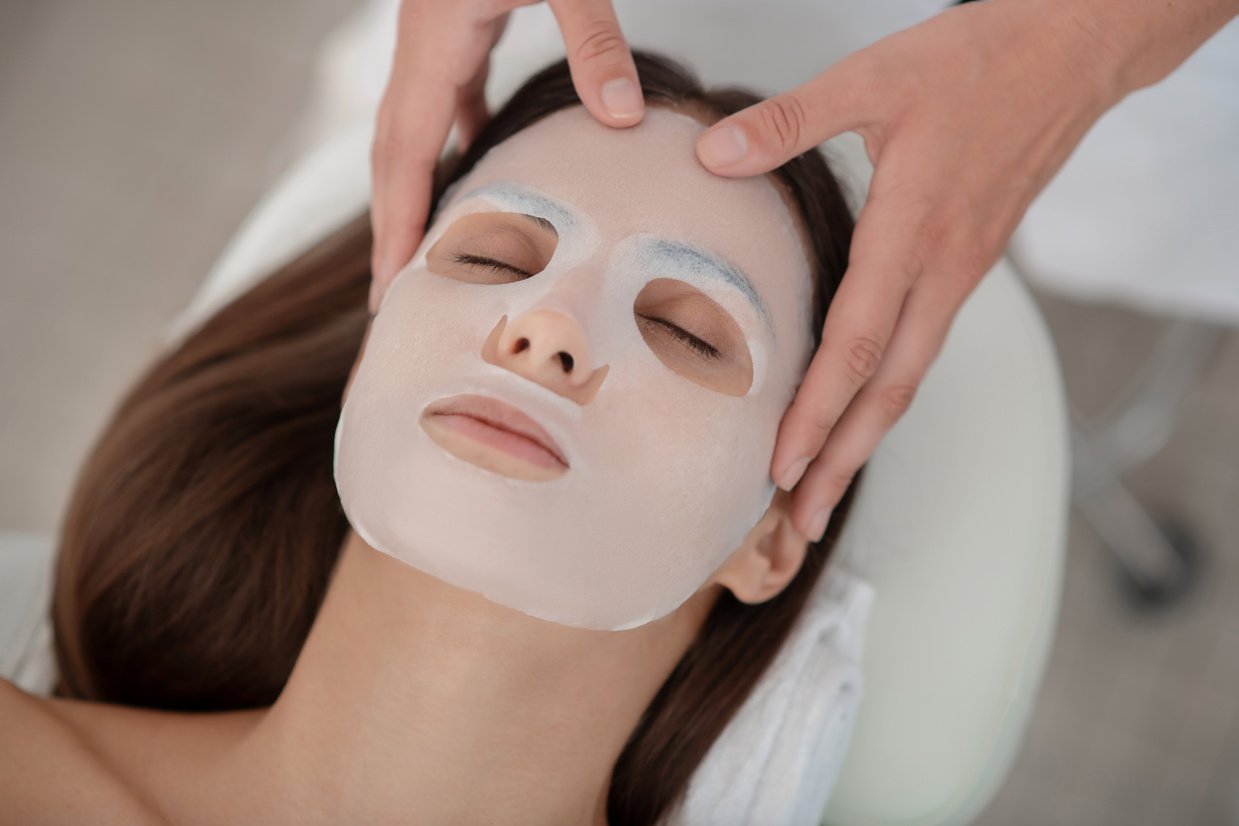 Beautician applying facial mask sheet on womans face